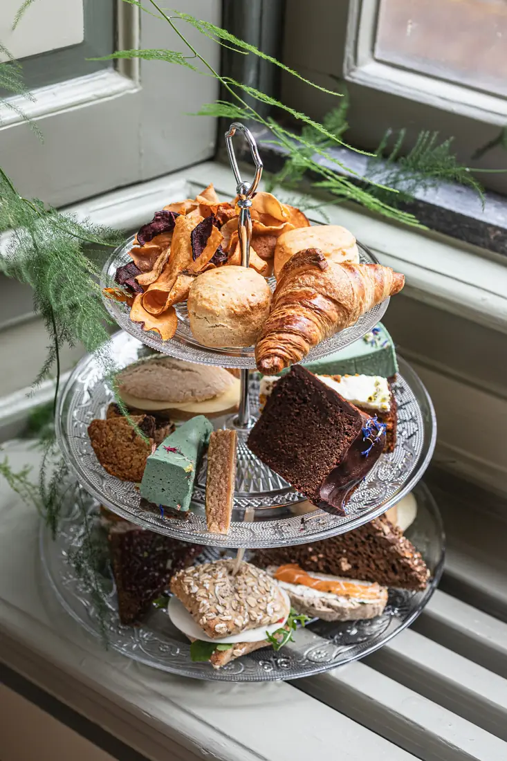 An afternoon tea stand with sandwiches and cakes by a window
